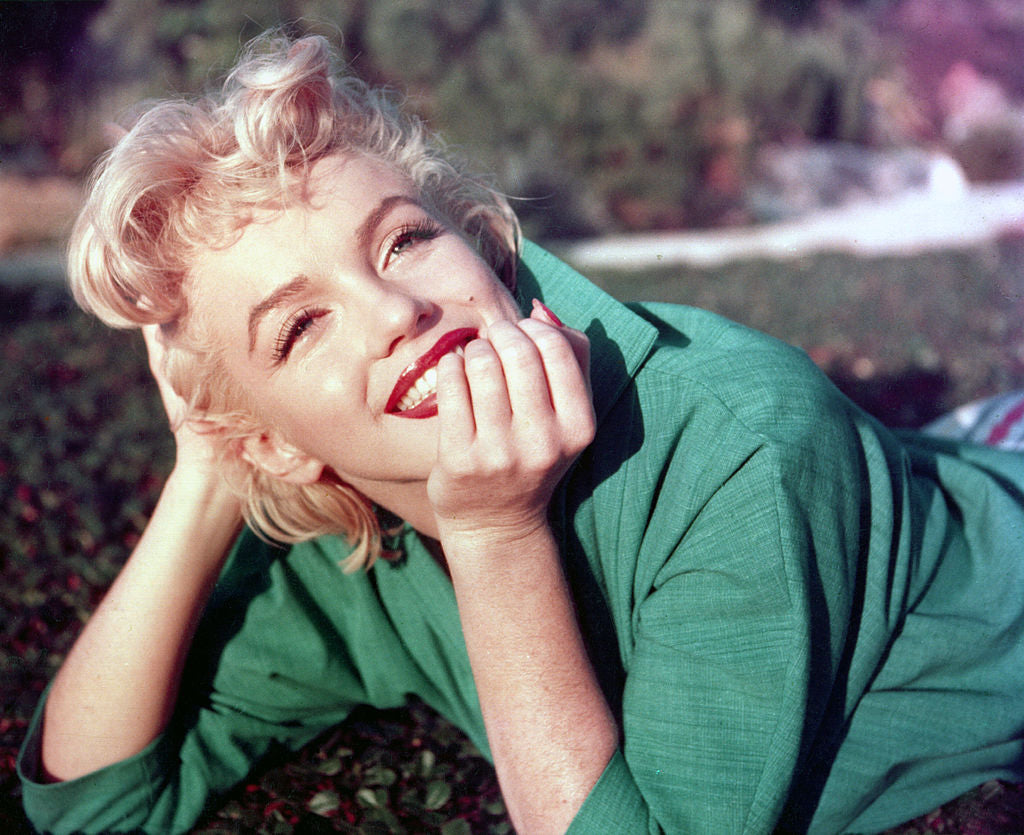 Colour photograph of a smiling Marilyn Monroe in a green top lying on the grass, chin resting on her hands, Palm Springs, 1954