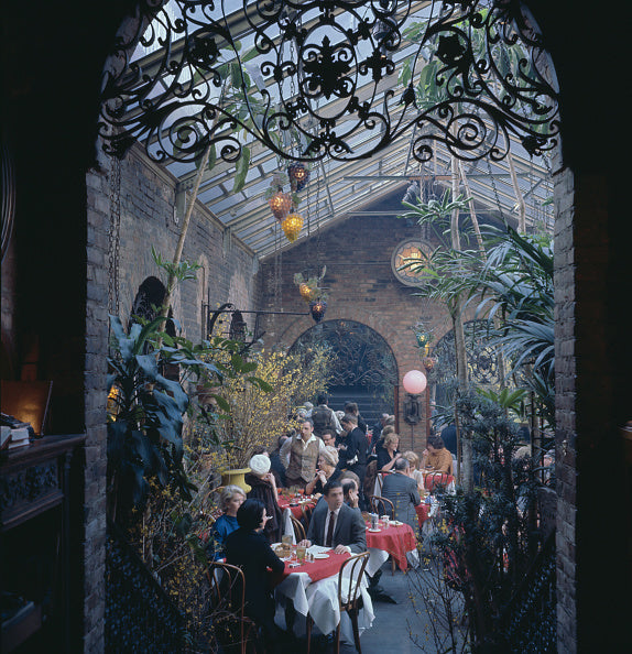 Colour photograph of diners at tables beneath an ornate iron and glass roof at The Sign of the Dove restaurant, New York, 1965