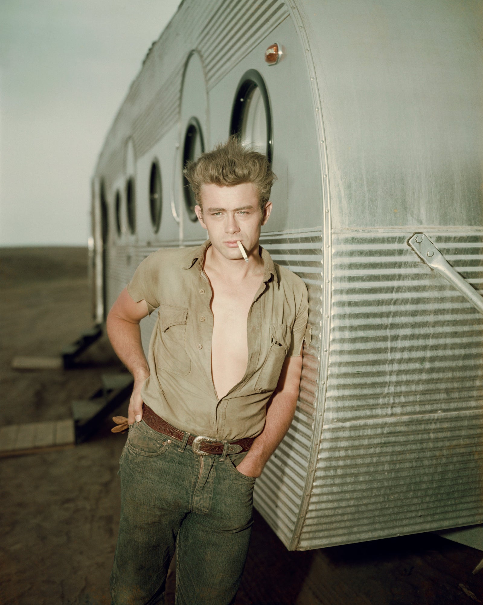 James Dean by Hulton Archive/Getty Images, 1955. American actor James Dean leaning against a dressing room trailer with his shirt open to the waist while smoking a cigarette on the set of director George Stevens's film, 'Giant,' in which he starred.. Open Edition C-Type Photographic Print. Portrait orientation. Available at Electric Gallery, London, UK.