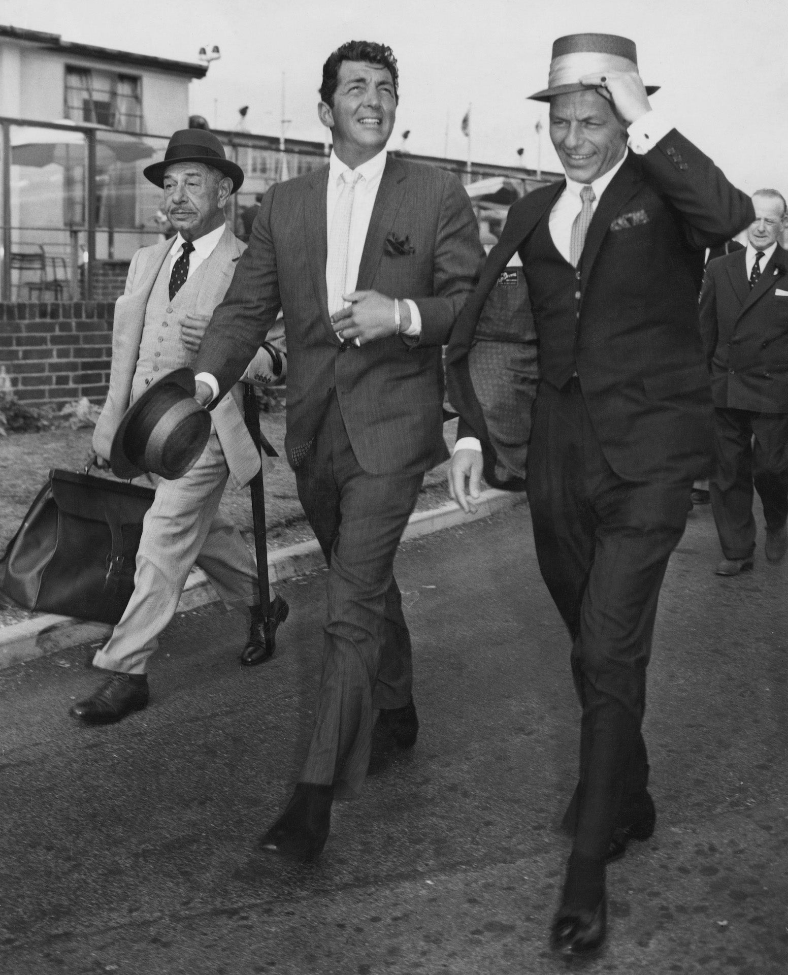 Martin And Sinatra by J. Wilds/Getty Images, 1961. American singers and actors Dean Martin and Frank Sinatra arriving at London airport, their friend and famed Beverly Hills restauranteur Mike Romanoff is with them.. Open Edition Resin Photographic Print. Portrait orientation. Available at Electric Gallery, London, UK.