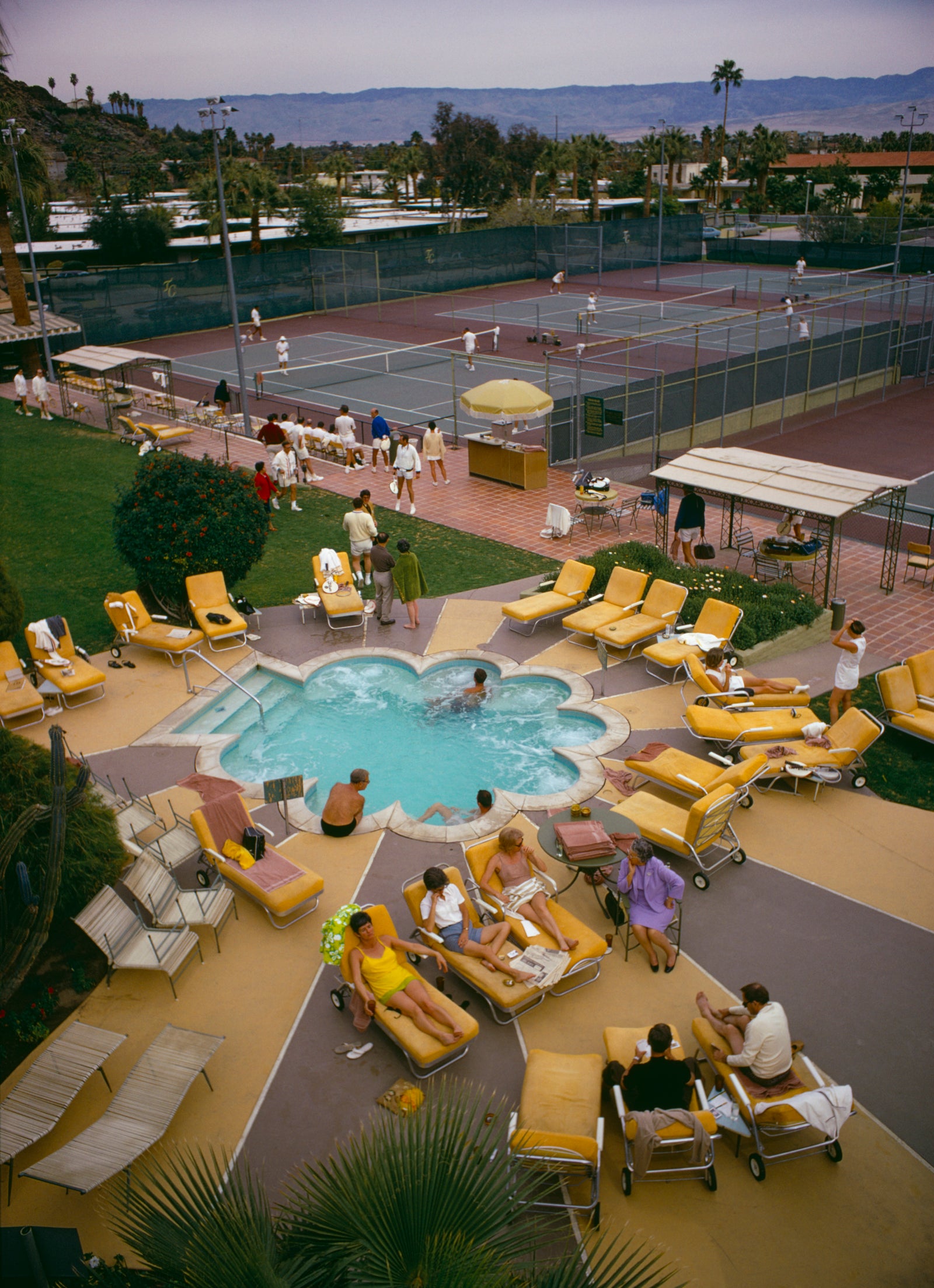 Relaxing At The Club by Slim Aarons/Getty Images, 1970. Members sunbathe around the pool at Palm Springs Tennis Club, California, circa. Open Edition C-Type Photographic Print.. Portrait orientation. Available at Electric Gallery, London, UK.