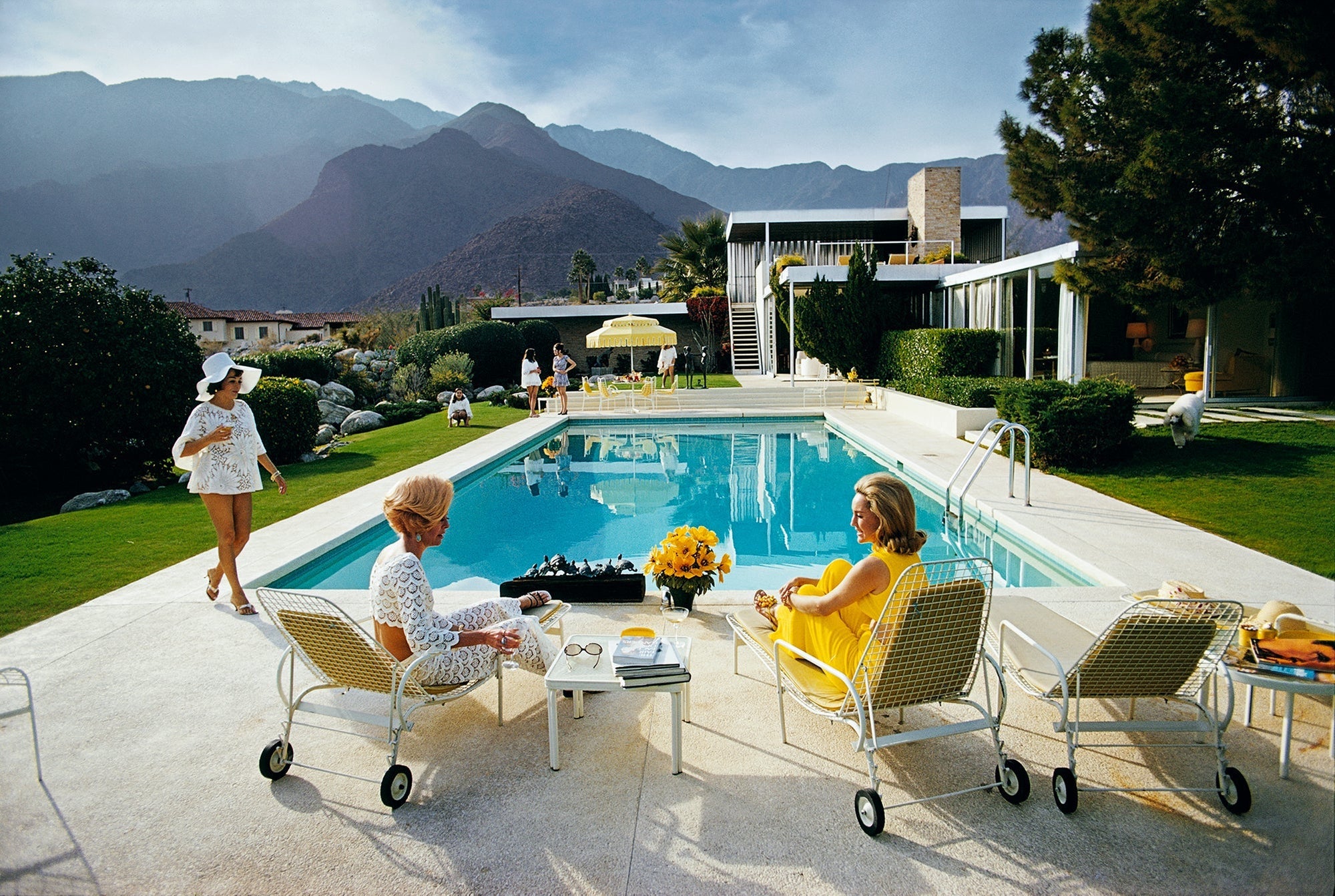 Catch Up By The Pool by Slim Aarons/Getty Images, 1970. Former fashion model Helen Dzo Dzo Kaptur, Nelda Linsk, wife of art dealer Joseph Linsk, and actress Lita Baron at the Kaufmann Desert House in Palm Springs, California. Open Edition C-Type Photographic Print. Landscape orientation. Available at Electric Gallery, London, UK.
