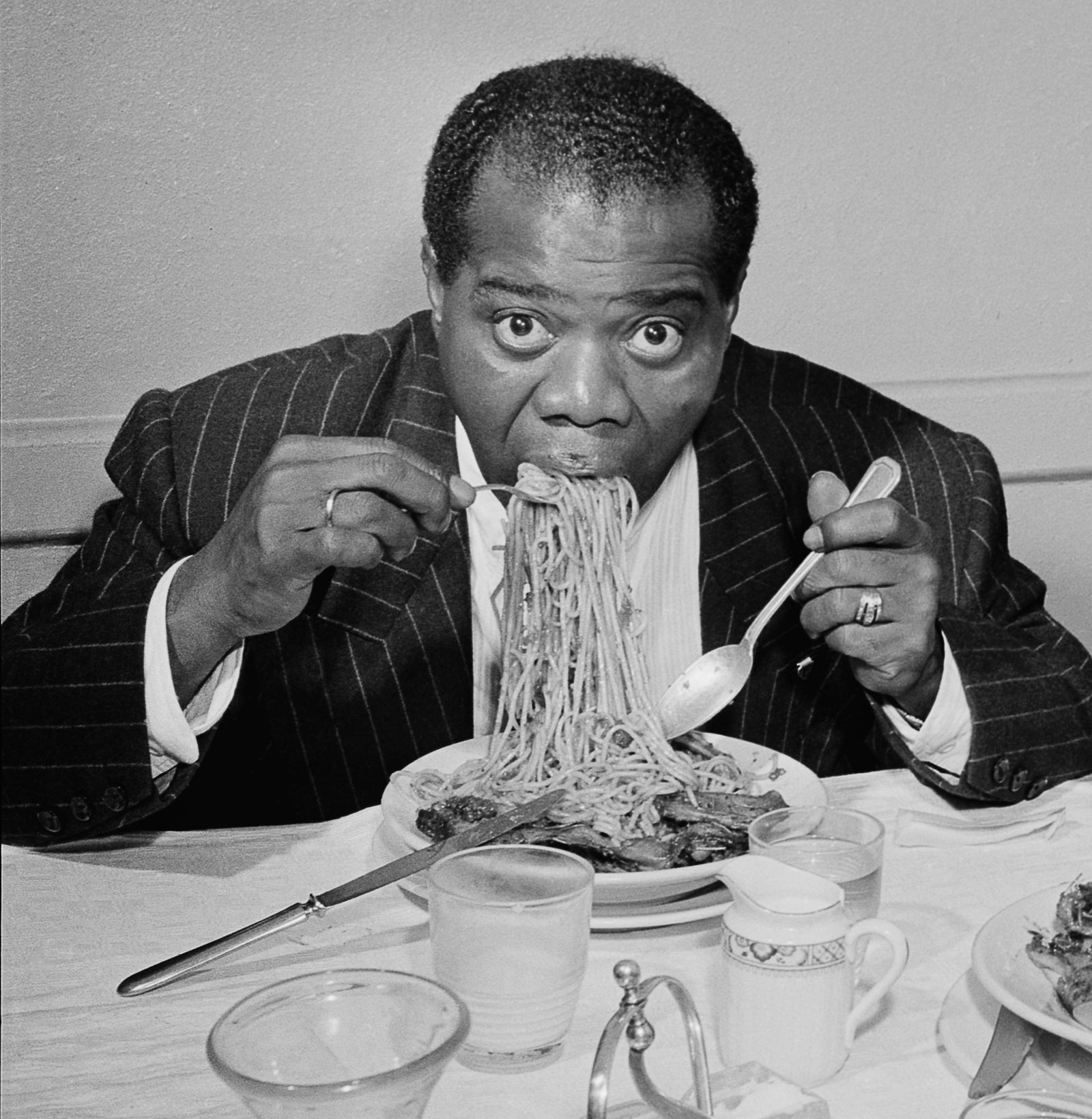 Dinner Jazz by Slim Aarons/Getty Images, 1949. American Jazz trumpeter and singer Louis Armstrong enjoys a plate of spaghetti in Rome.. Open Edition C-Type Photographic Print. Square orientation. Available at Electric Gallery, London, UK.
