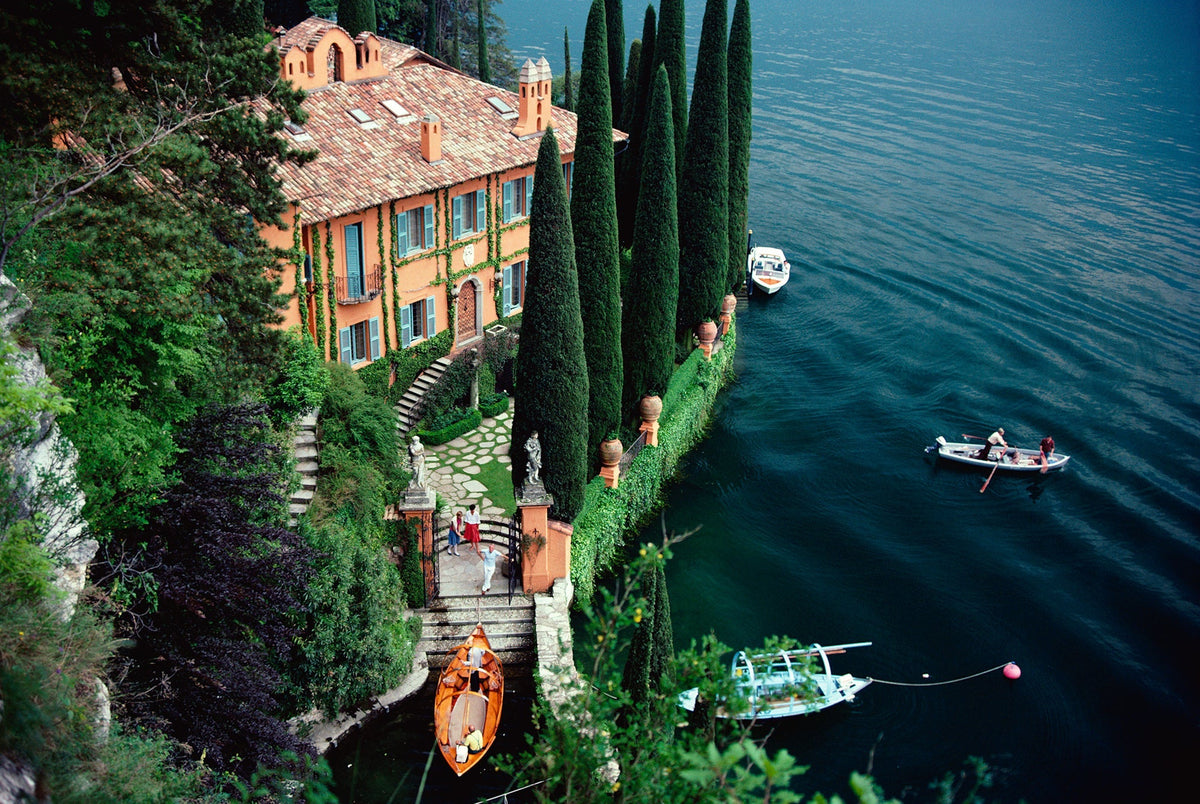 Giacomo Montegazza by Slim Aarons/Getty Images, 1983. Giacomo and Stefania Montegazza welcome guests arriving by boat at their villa, La Cassinella, on Lake Como. Open Edition C-Type Photographic Print. Landscape orientation. Available at Electric Gallery, London, UK.