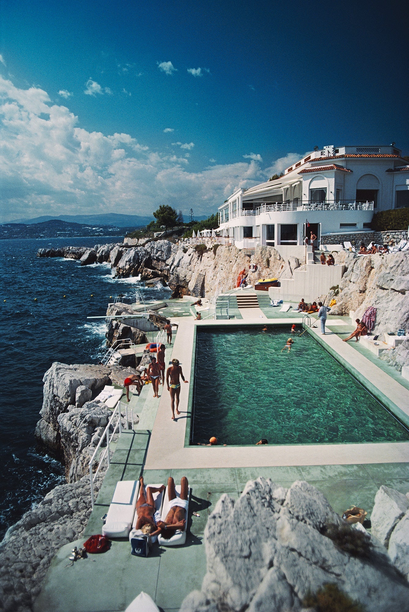 Hotel Du Cap-Eden-Roc by Slim Aarons/Getty Images, 1976. Guests by the pool at the Hotel du Cap Eden-Roc, Antibes, France. Open Edition C-Type Photographic Print. Portrait orientation. Available at Electric Gallery, London, UK.