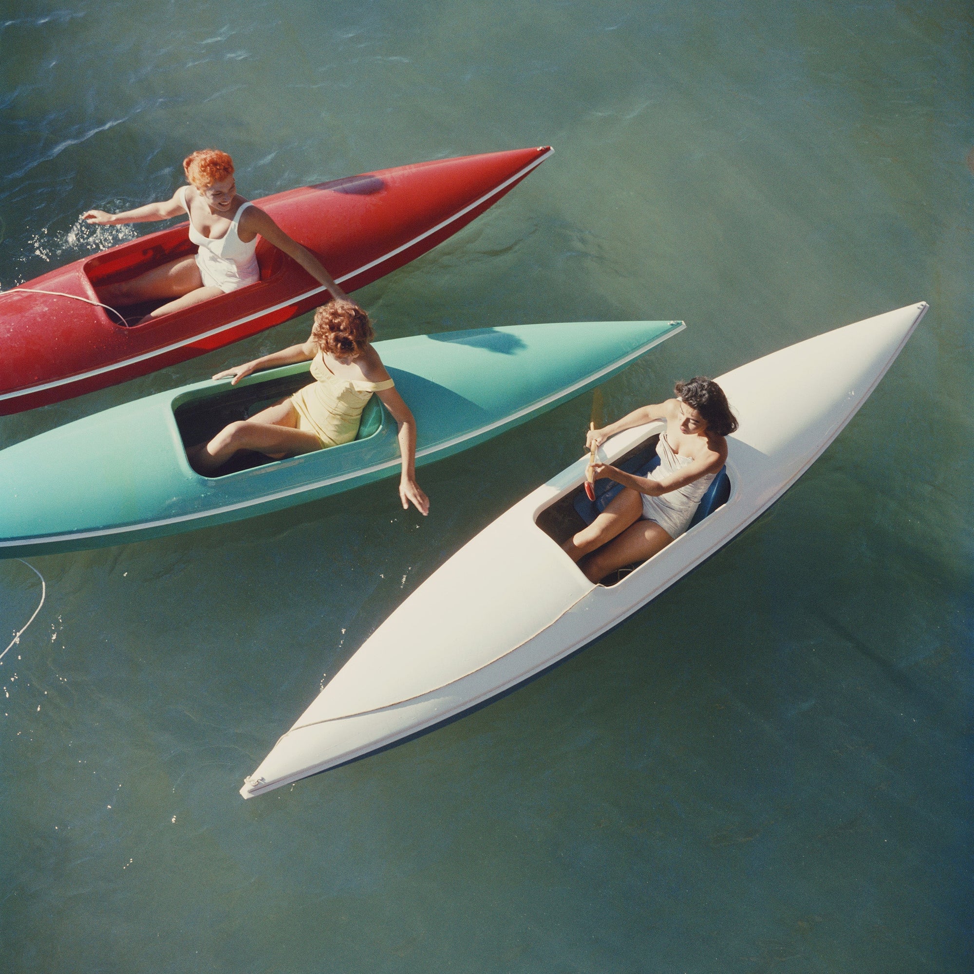 Lake Tahoe Trip by Slim Aarons/Getty Images, 1959. Young women canoeing at Zephyr Cove on the Nevada side of Lake Tahoe, USA. Open Edition C-Type Photographic Print. Square orientation. Available at Electric Gallery, London, UK.