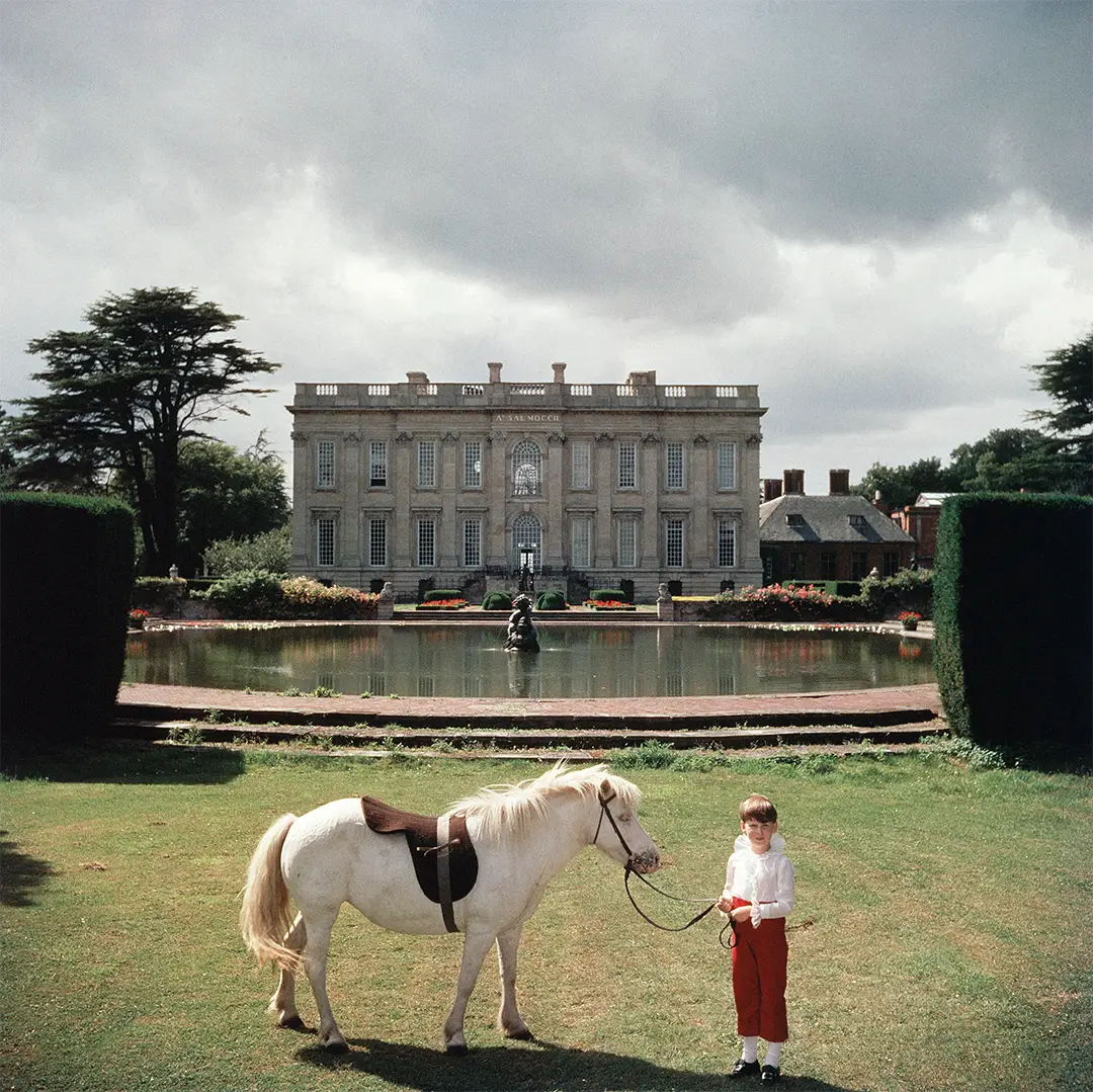Lord Of All I Survey by Slim Aarons/Getty Images, 1957. The youngest peer in England, seven year old Thomas Alexander Fermor-Hesketh, 3rd Baron and 10th Baronet Hesketh with his pony 'Blossom' by the lake in the magnificent grounds of his ancestral home, Easton Neston House in Northamptonshire.. Open Edition C-Type Photographic Print. Square orientation. Available at Electric Gallery, London, UK.