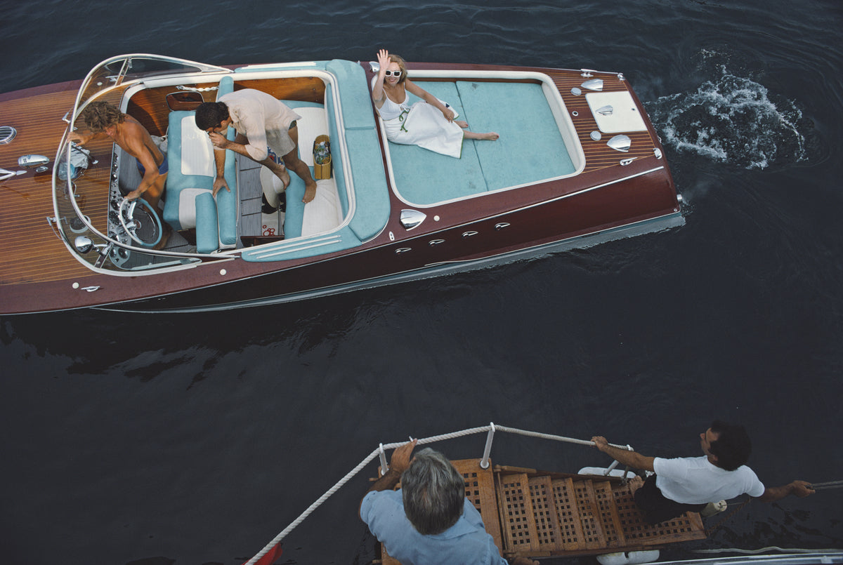 Monte Carlo by Slim Aarons/Getty Images, 1975. Friends board a riva boat in Monte Carlo, Monaco. Open Edition C-Type Photographic Print. Landscape orientation. Available at Electric Gallery, London, UK.