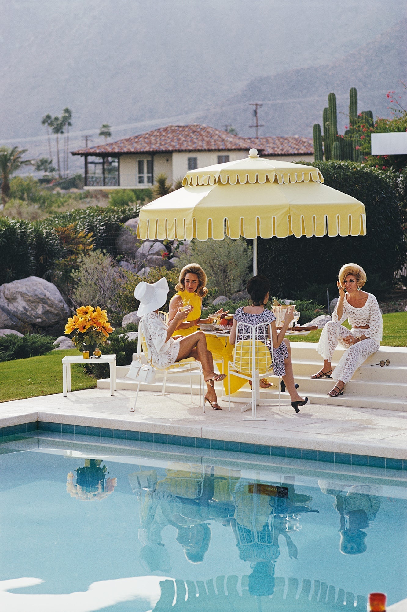 Nelda And Friends by Slim Aarons/Getty Images, 1970. Ladies by the pool at the Kaufmann Desert House in Palm Springs, California. Open Edition C-Type Photographic Print. Portrait orientation. Available at Electric Gallery, London, UK.