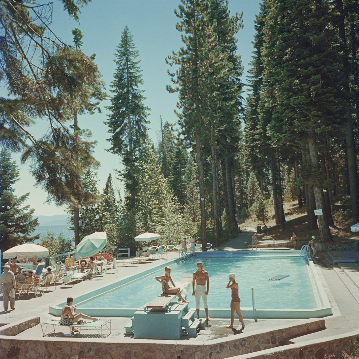 Pool At Lake Tahoe by Slim Aarons/Getty Images, 1959. Bathers by a pool at the Tahoe Tavern on the shore of Lake Tahoe, California. Open Edition C-Type Photographic Print. Square orientation. Available at Electric Gallery, London, UK.