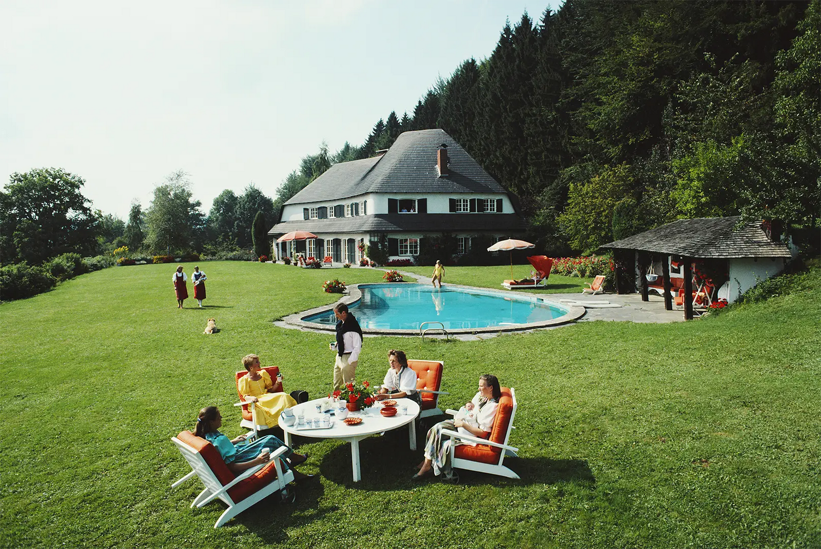 Von Oswald House by Slim Aarons/Getty Images, 1986. A group of people relax in the garden at the house of Johanna Von Oswald. Open Edition C-Type Photographic Print.. Portrait orientation. Available at Electric Gallery, London, UK.