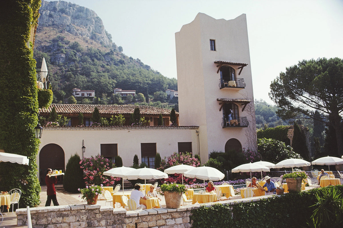 Breakfast on the verandah of the Chateau Saint-Martin, a luxury hotel in Vence on the Cote d'Azur, France, 1986. The building was once a Commanderie of the Knights Templar, dating back to the 12th century. Slim Aarons photograph.