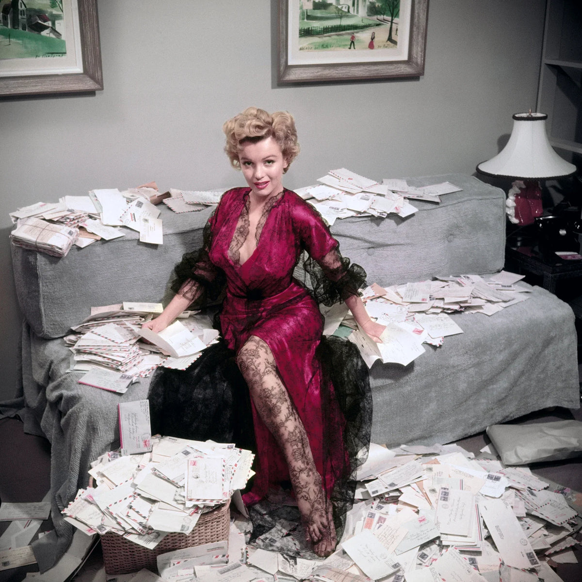 Marilyn Monroe, wearing a red negligee trimmed with black lace, sorts out her fan mail shortly after her film 'The Asphalt Jungle' had been released. Slim Aarons photograph.