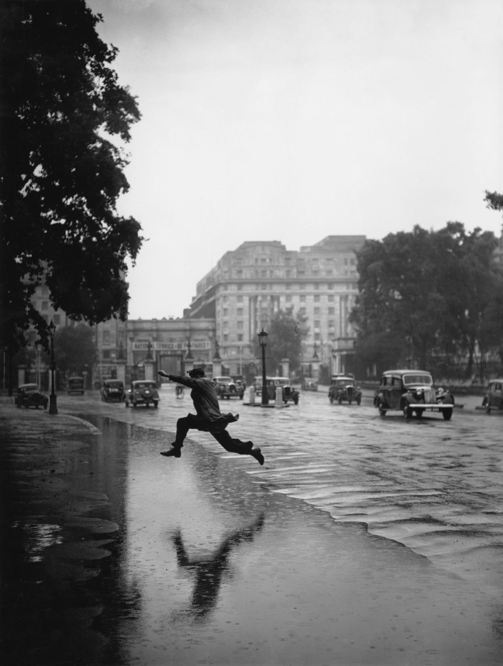 Flooded Road by J. A. Hampton/Getty Images, 1939. A pedestrian attempts to leap across a flooded road near Hyde Park in London, 3rd. Open Edition Resin Photographic Print. Landscape orientation. Available at Electric Gallery, London, UK.